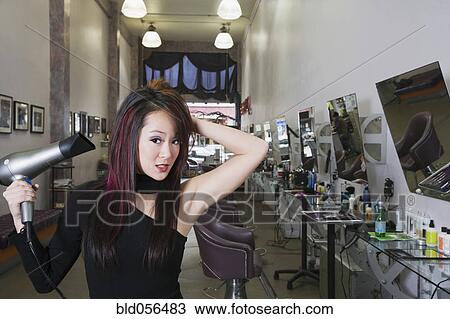 Stock Image - Asian hair stylist blow drying hair. Fotosearch