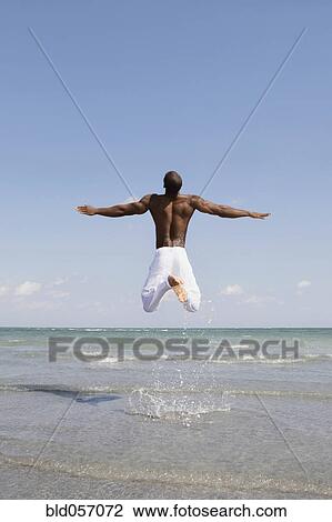 Stock Image - Bare-chested man jumping in ocean surf. Fotosearch