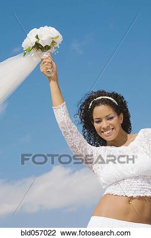 Stock Image - Hispanic bride holding bouquet over head. Fotosearch