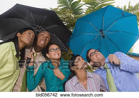 Stock Image - Hispanic businesspeople standing under umbrellas. Fotosearch