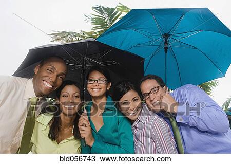 Stock Image - Hispanic businesspeople standing under umbrellas. Fotosearch