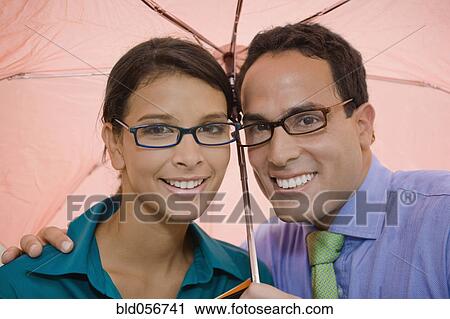 Stock Image - Hispanic couple standing under umbrella. Fotosearch