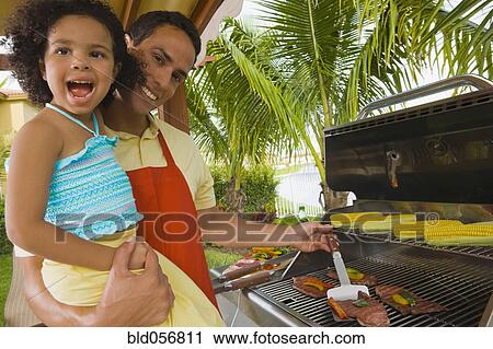 Stock Image - Hispanic father and daughter barbecuing. Fotosearch