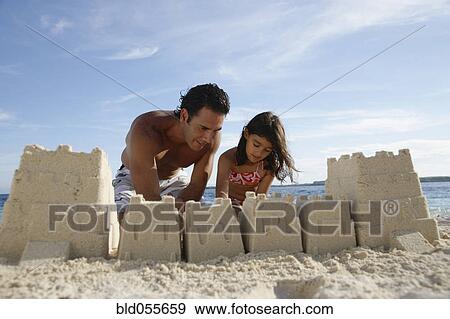 Stock Photo - Hispanic father and daughter building sand castle. Fotosearch
