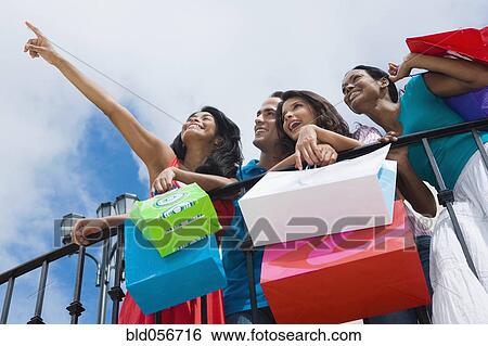 Stock Photograph - Hispanic friends holding shopping bags. Fotosearch