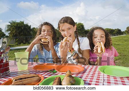 Stock Image - Hispanic girls eating at picnic table. Fotosearch