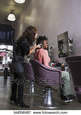Stock Photo - Hispanic hair stylist styling African woman’s hair. Fotosearch