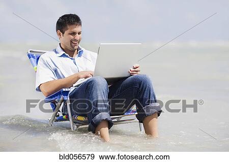 Hispanic man in beach chair with laptop View Large Photo Image Stock Photo - Hispanic man in beach chair with laptop . Fotosearch