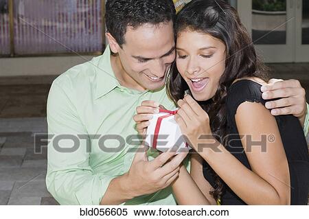 Stock Photography - Hispanic man surprising girlfriend with gift. Fotosearch