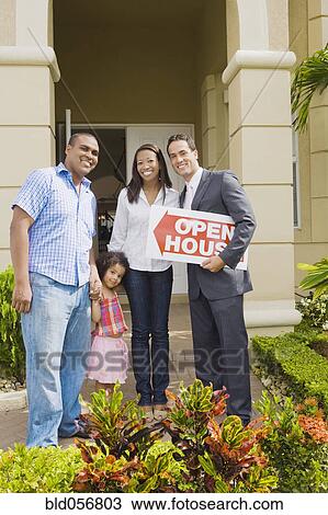 Stock Image - Hispanic real estate agent and African family in front of house. Fotosearch