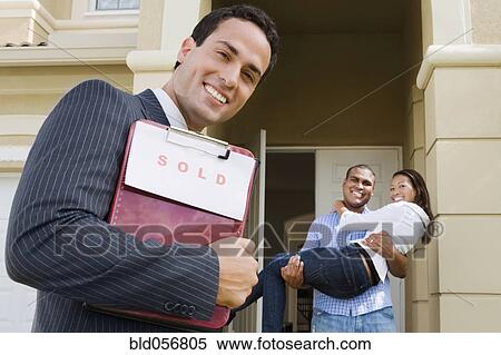 Stock Photography - Hispanic real estate agent and African couple in front of house. Fotosearch