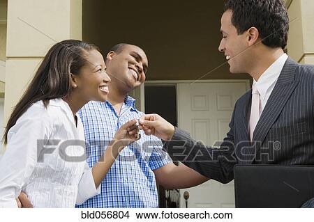Picture - Hispanic real estate agent handing house key to African couple. Fotosearch