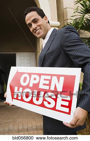 Stock Image - Hispanic real estate agent holding Open House sign. Fotosearch