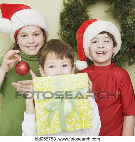 Stock Image - Hispanic siblings in Santa Claus hats with gift. Fotosearch