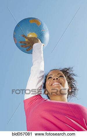 Stock Image - Hispanic woman holding globe ball. Fotosearch