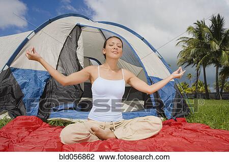 Stock Image - Hispanic woman meditating in front of tent. Fotosearch