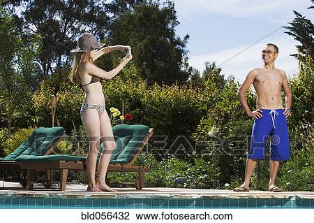 Stock Image - Hispanic woman taking photograph of boyfriend. Fotosearch