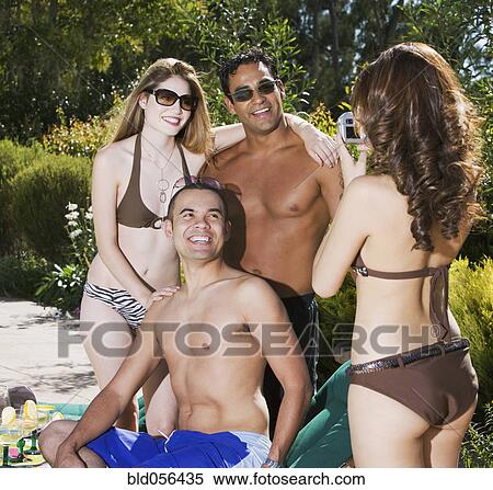Stock Photography - Hispanic woman taking photograph of friends. Fotosearch