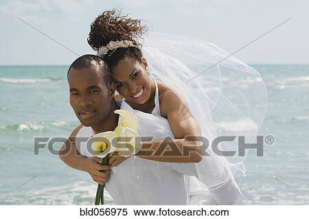 Stock Photography - Multi-ethnic bride and groom hugging at beach. Fotosearch