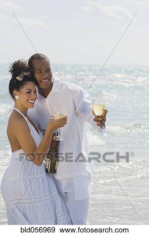 Stock Photo - Multi-ethnic couple drinking wine at beach. Fotosearch