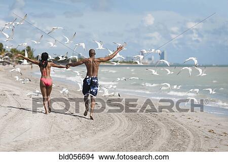 Picture - Multi-ethnic couple holding hands at beach. Fotosearch