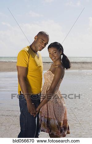 Stock Image - Multi-ethnic couple holding hands at beach. Fotosearch