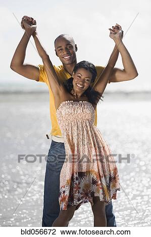 Stock Image - Multi-ethnic couple holding hands at beach. Fotosearch