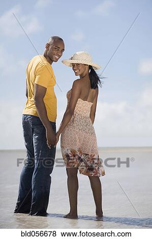 Stock Photo - Multi-ethnic couple holding hands at beach. Fotosearch