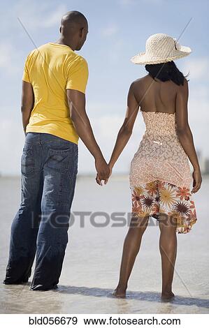 Stock Photo - Multi-ethnic couple holding hands at beach. Fotosearch