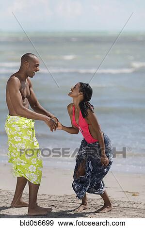 Stock Photo - Multi-ethnic couple holding hands at beach. Fotosearch