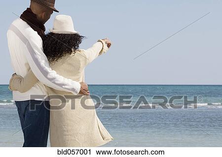 Multi-ethnic couple hugging and pointing at beach View Large Photo Image Stock Image - Multi-ethnic couple hugging and pointing at beach. Fotosearch