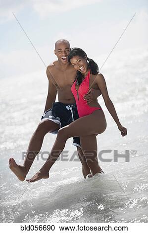 Stock Image - Multi-ethnic couple hugging at beach. Fotosearch