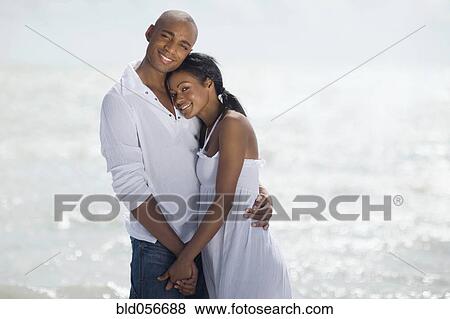 Stock Photo - Multi-ethnic couple hugging at beach. Fotosearch