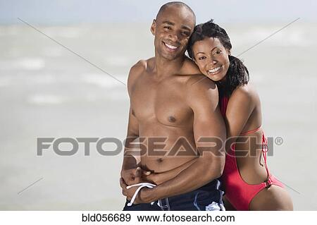 Stock Photo - Multi-ethnic couple hugging at beach. Fotosearch
