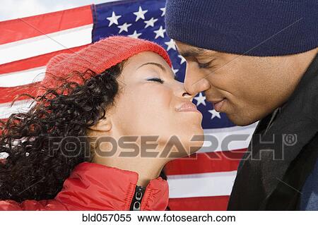 Stock Photography - Multi-ethnic couple kissing in front of American flag. Fotosearch