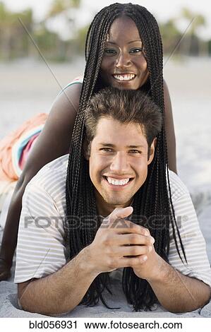 Stock Image - Multi-ethnic couple laying on beach. Fotosearch