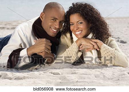 Stock Photo - Multi-ethnic couple laying on beach. Fotosearch