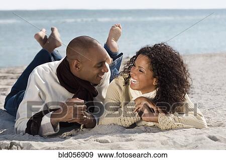 Stock Photo - Multi-ethnic couple laying on beach. Fotosearch