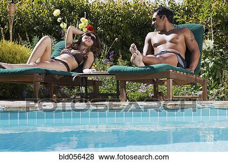 Stock Photo - Multi-ethnic couple relaxing next to swimming pool. Fotosearch
