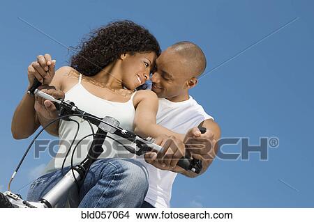 Multi-ethnic couple sitting on bicycle View Large Photo Image Picture - Multi-ethnic couple sitting on bicycle. Fotosearch