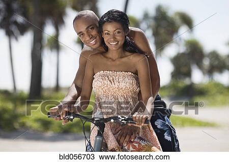 Stock Image - Multi-ethnic couple sitting on bicycle. Fotosearch