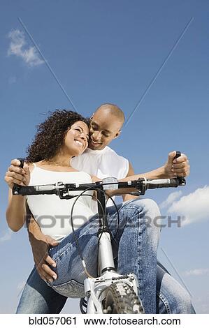 Stock Image - Multi-ethnic couple sitting on bicycle. Fotosearch
