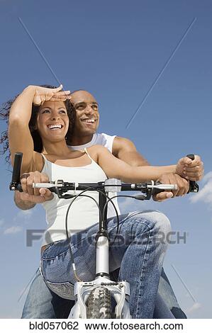 Stock Image - Multi-ethnic couple sitting on bicycle. Fotosearch