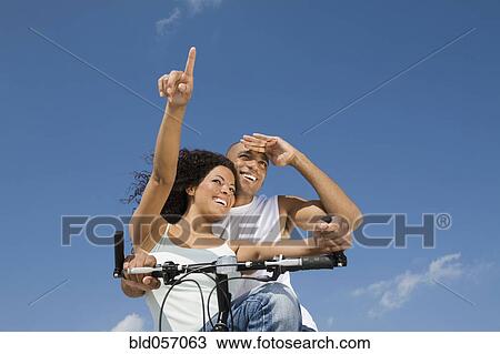 Multi-ethnic couple sitting on bicycle View Large Photo Image Stock Image - Multi-ethnic couple sitting on bicycle. Fotosearch