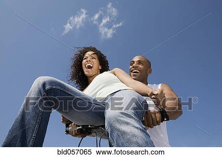 Stock Photography - Multi-ethnic couple sitting on bicycle. Fotosearch