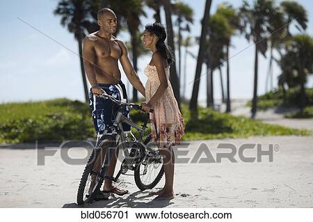 Stock Image - Multi-ethnic couple with bicycle at beach. Fotosearch
