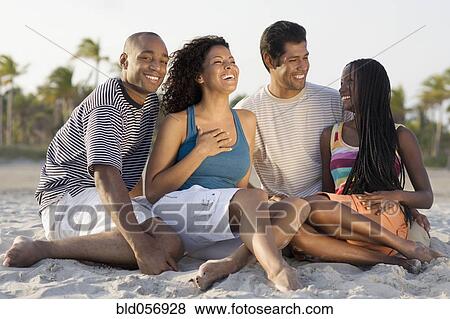 Stock Photo - Multi-ethnic couples sitting on beach. Fotosearch