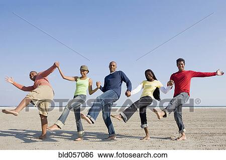 Stock Photograph - Multi-ethnic friends holding hands and kicking. Fotosearch