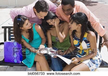 Stock Image - Multi-ethnic friends looking at magazine. Fotosearch