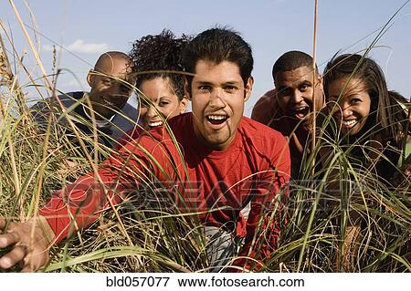 Stock Photo - Multi-ethnic friends looking through tall grass. Fotosearch